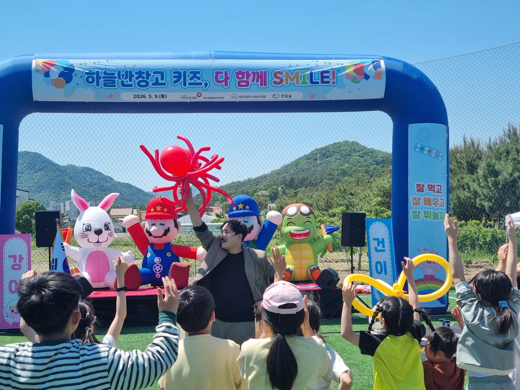 야외 축제에서 풍선 캐릭터와 함께 호응하는 아이들