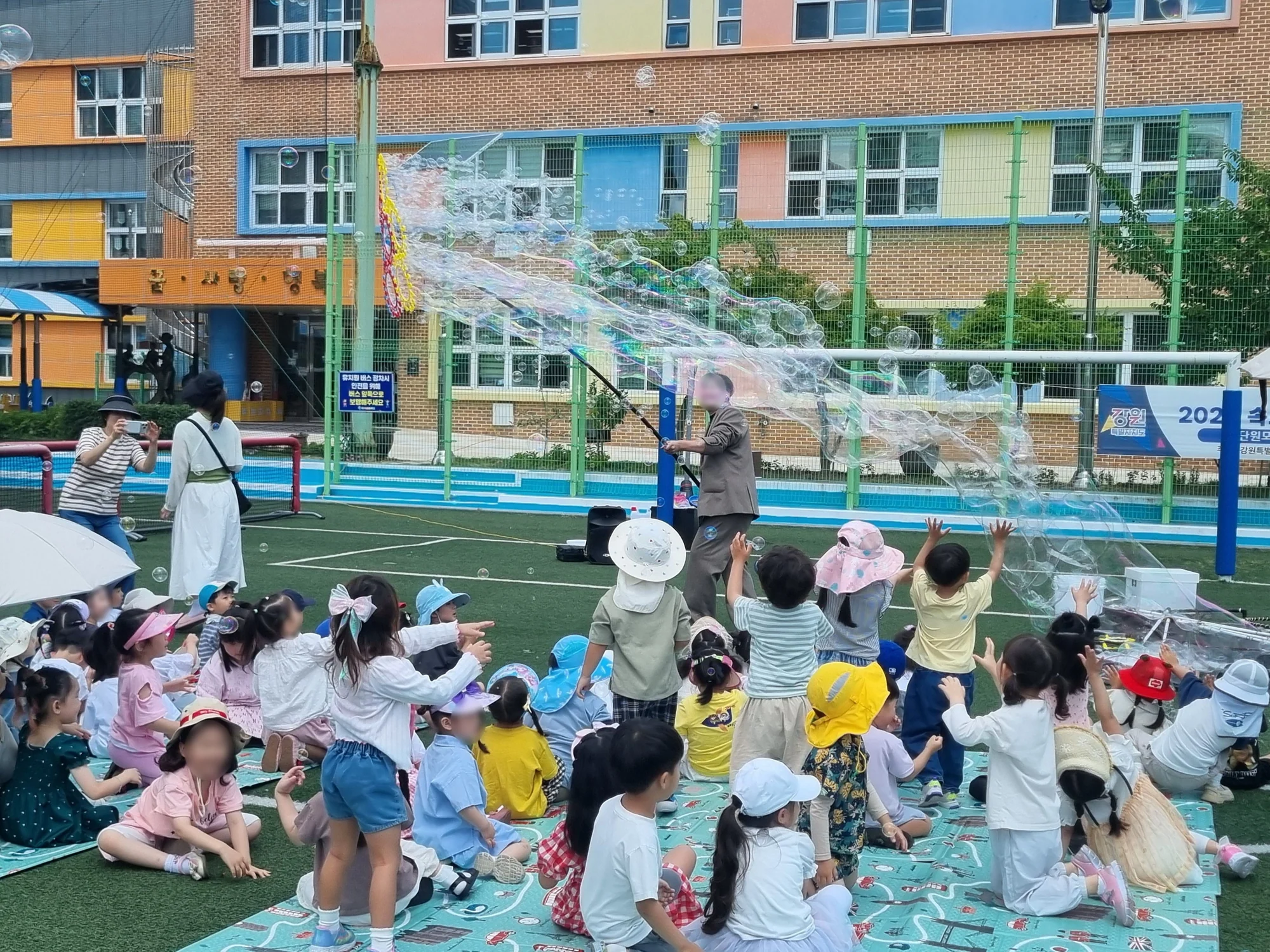 잔디 운동장에 앉은 아이들 위로 퍼지는 비눗방울